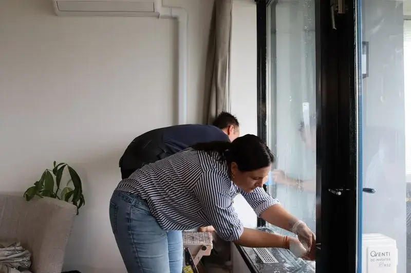 Twee mensen plaatsen isolatiefolie op een raam als onderdeel van woningisolatie